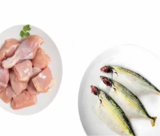 Plate of chicken curry cut pieces beside two cleaned big mackerel on a white dish