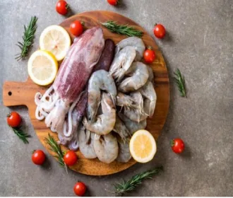 Whole squid and white prawns arranged on a wooden board with lemon and tomatoes